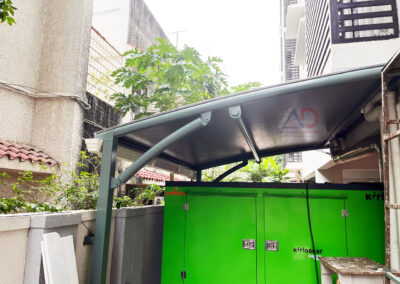 Tensile sun shade shelter over green generator unit in residential building by Amudha Decors