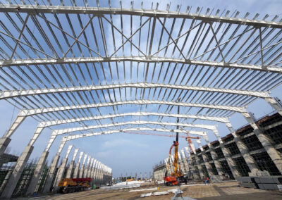 PEB steel structure roofing framework construction by Amudha Decors at Mahabalipuram industrial project site with curved steel trusses and large warehouse structure.