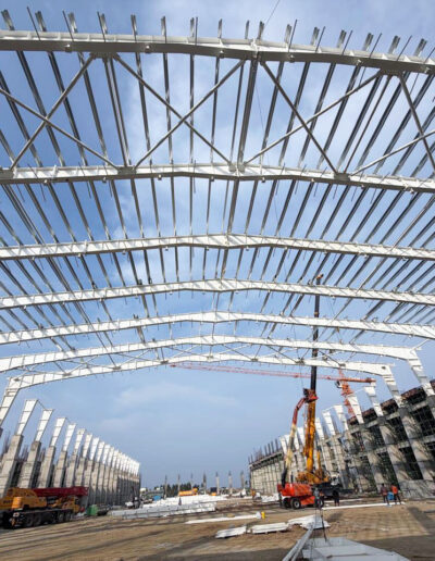 PEB steel structure roofing framework construction by Amudha Decors at Mahabalipuram industrial project site with curved steel trusses and large warehouse structure.