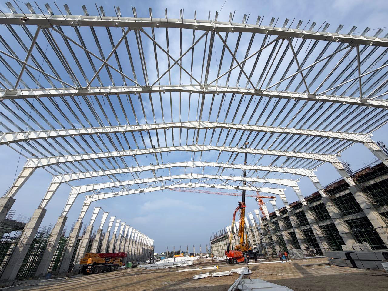 PEB steel structure roofing framework construction by Amudha Decors at Mahabalipuram industrial project site with curved steel trusses and large warehouse structure.