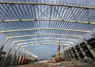 PEB steel structure roofing framework construction by Amudha Decors at Mahabalipuram industrial project site with curved steel trusses and large warehouse structure.