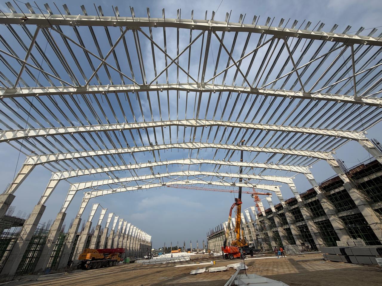 Premium PEB Steel Structure Construction in Mahabalipuram | Amudha Decors PEB steel structure roofing framework construction by Amudha Decors at Mahabalipuram industrial project site with curved steel trusses and large warehouse structure.
