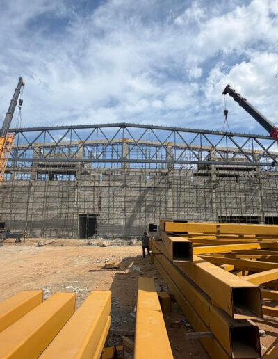 Pre Engineered Building (PEB) steel structure installation using cranes at an industrial construction site in Chennai by Amudha Decors.