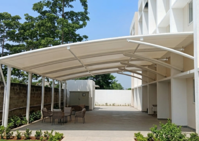 White tensile membrane car parking canopy installed beside a commercial building by Amudha Decors, providing durable weather protection and modern architectural design in Chennai.