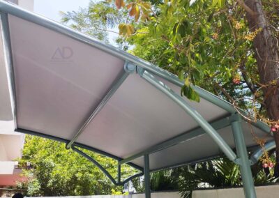 Fabric canopy with curved tubular metal supports installed beside a building, providing outdoor shade and weather protection.