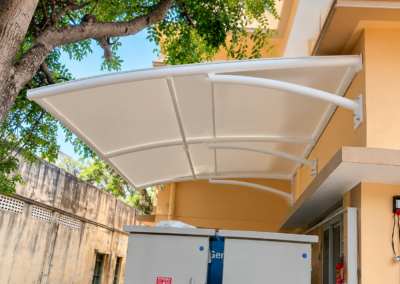 White tensile canopy installed above outdoor electrical equipment at a building